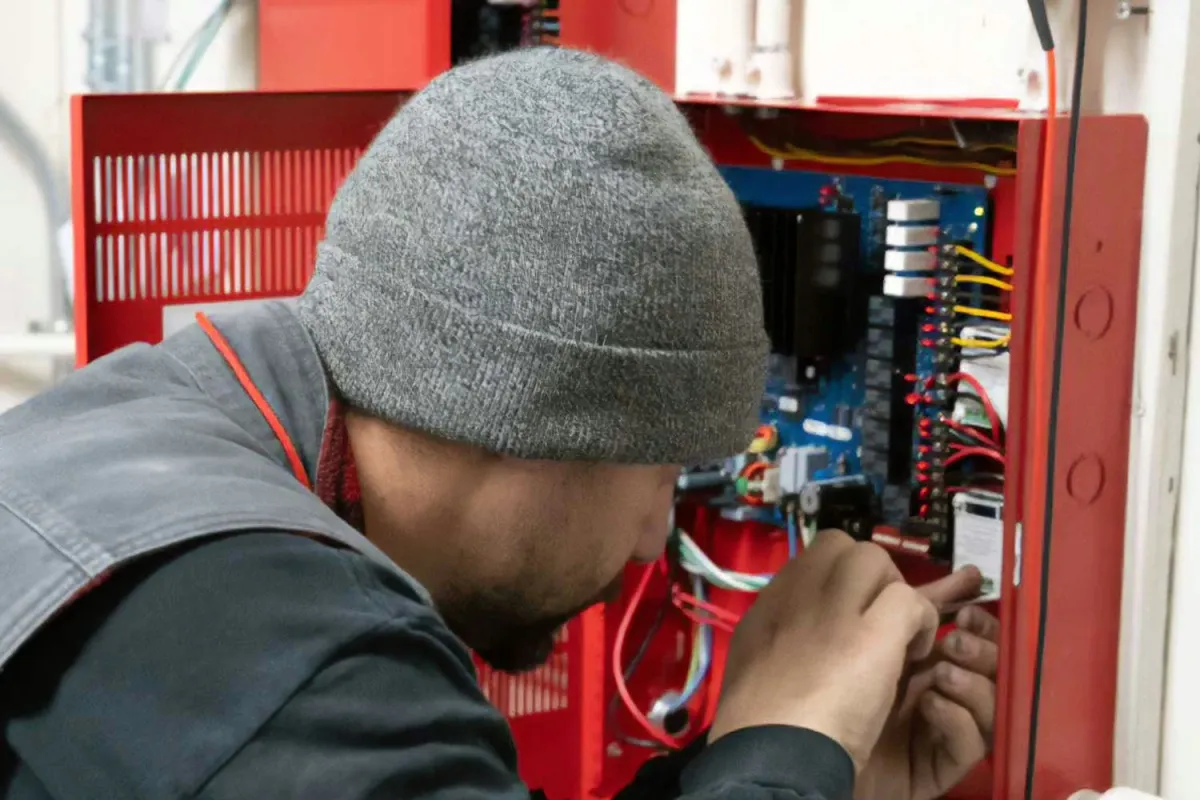 State Fire technician performing low voltage fire alarm system installation in a commercial facility for fire protection and life safety compliance.