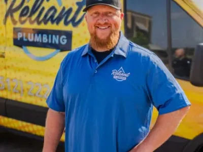 Reliant Plumbing employee posing in uniform in from of a yello work truck