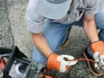 Worker kneeling down looking at the screen of a residential sewer camera