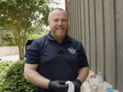 max hicks, owner of reliant plumbing, standing outside of a building holding a rag and smiling