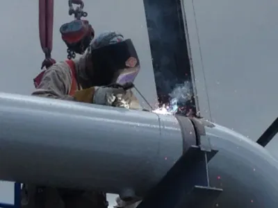 Close Up Of Person Wearing Safety Mask Welding On Metal Pipe