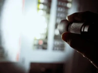 Electrician inspecting residential electrical panel with flashlight during emergency repair.