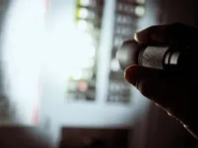 Electrician inspecting residential electrical panel with flashlight during emergency repair.