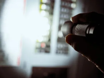 Electrician inspecting residential electrical panel with flashlight during emergency repair.