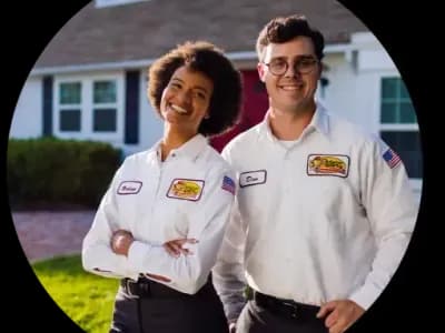 Two electricians in uniform smiling in front of a home.