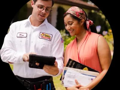 Electrician in uniform showing a customer a tablet, smiling, and standing in front of a home.