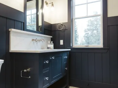 A modern bathroom featuring a black vanity with a white marble countertop and a built-in backsplash. The vanity includes multiple drawers with silver knobs and an open shelf beneath.