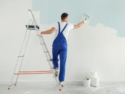 Painter in blue overalls painting a wall white.