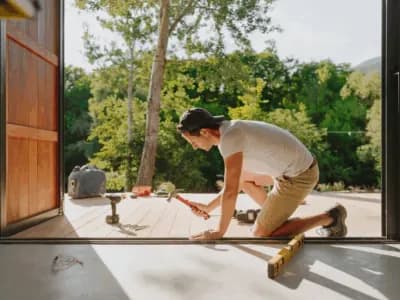 Person hammering nails on wooden deck outside.
