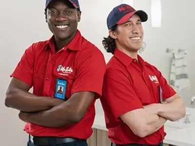 Two Mr. Rooter professionals standing back to back with their arms crossed.
