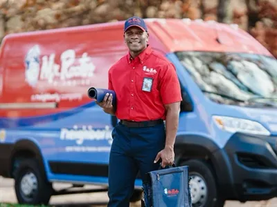 Mr. Rooter professional standing beside a branded work van.