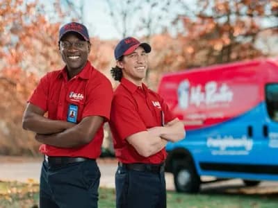 Two Mr. Rooter professionals standing back to back beside a branded van.