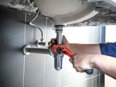 Plumber uses wrench to repair water pipe under sink There is maintenance to fix the water leak in the bathroom.with red wrench, plumbing install concept.