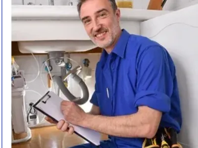 Plumbing technician checking water installation under the sink of a home kitchen with notepad.