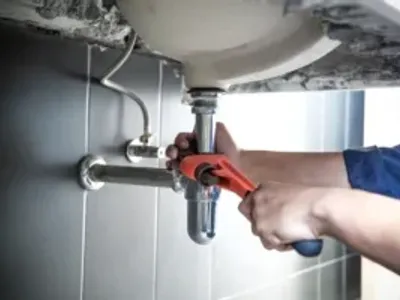 Plumber uses wrench to repair water pipe under sink There is maintenance to fix the water leak in the bathroom.with red wrench, plumbing install concept.