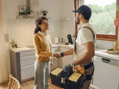 Professional repairman in uniform shaking hands with woman while standing at home kitchen