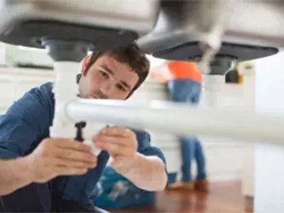 Plumber working on pipes under sink