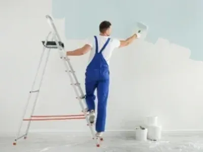 Painter in blue overalls painting a wall white.