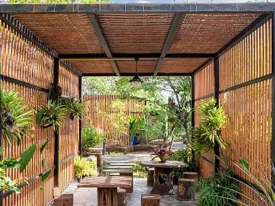 Outdoor pergola with wooden furniture and plants.