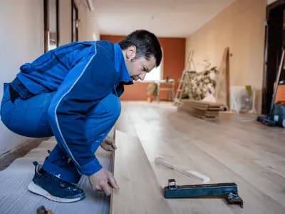 Man installing laminate flooring in room.