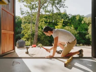 Person hammering nails on wooden deck outside.