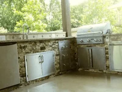 Outdoor kitchen featuring custom stone cabinetry, stainless steel appliances, and a grill, designed for functionality and style in home remodeling.