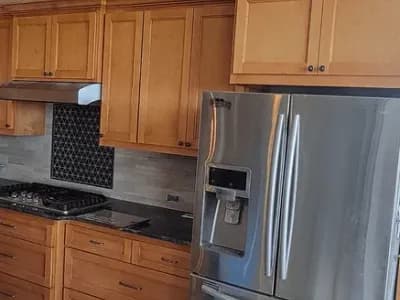 Custom kitchen cabinetry with wooden cabinets, modern stainless steel refrigerator, and gas stove, showcasing Ace Kustoms' craftsmanship and design expertise in home remodeling.