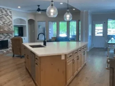 Modern kitchen with custom cabinetry, large island, quartz countertop, pendant lighting, and open layout connecting to living area and outdoor space.