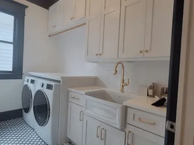 Modern laundry room design featuring white cabinetry, gold fixtures, dual washing machines, and a farmhouse sink, emphasizing custom cabinetry solutions for enhanced home functionality.