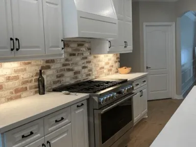 Modern kitchen featuring white cabinetry, stainless steel appliances, and a brick backsplash, showcasing custom woodworking craftsmanship by Ace Kustoms Cabinets & Trim.