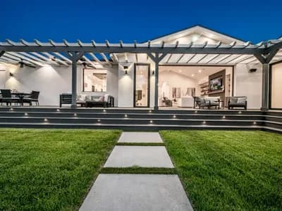 A covered outdoor living space with a wood-plank ceiling, recessed lighting, and a modern seating area overlooking a backyard.