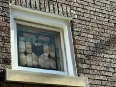 Stained glass window framed by new window wrap flashing on brick exterior, showcasing meticulous installation for weatherproofing.