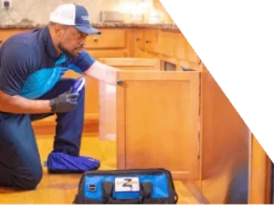 Z PLUMBERS worker kneeling and shining light under cabinet