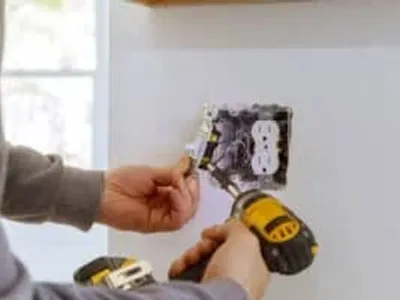 Person installing an electrical outlet with a drill and screwdriver.