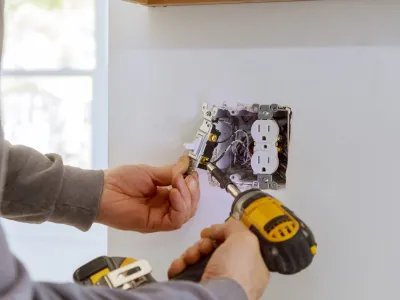 Person installing an electrical outlet with a drill and screwdriver.