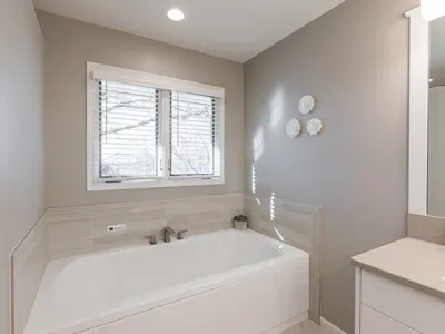 Newly renovated bathroom with a large white bathtub and a tan granite sink counter top