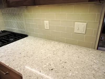 Remodeled kitchen with green bricks on the walls and with white granite countertops