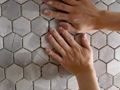 Hands installing hexagonal mosaic tile on a wall.