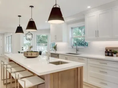 Bright modern kitchen with white cabinets, large island, pendant lights, and light wood flooring.