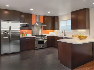Modern kitchen remodel with dark espresso cabinets, stainless steel appliances, white quartz countertops, and an orange accent wall.