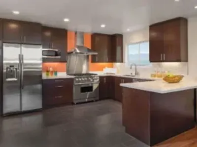 Modern kitchen remodel with dark espresso cabinets, stainless steel appliances, white quartz countertops, and an orange accent wall.