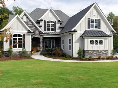 Craftsman-style home exterior with board and batten siding, stone accents, dark roof, and manicured lawn.
