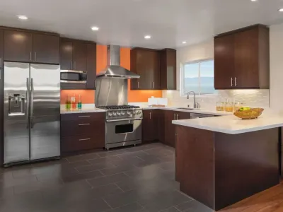 Modern kitchen remodel with dark espresso cabinets, stainless steel appliances, white quartz countertops, and an orange accent wall.