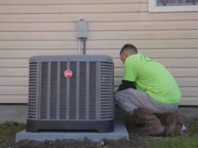 Technician in green shirt performing maintenance on a Rheem air conditioning unit outside a home, highlighting Tillman's Services' expertise in HVAC repair and installation in Gulfport, MS.