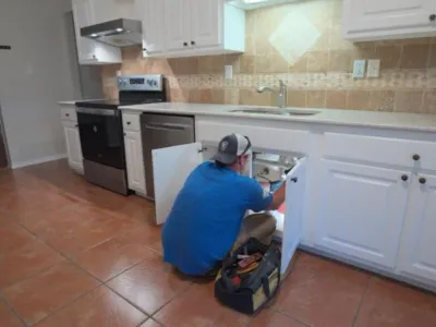 Plumber inspecting under kitchen sink for repairs in residential space, highlighting plumbing services in Gulfport, MS.
