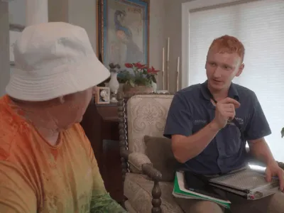 Technician discussing HVAC financing options with a customer in a cozy living room setting, featuring a clipboard and documents for reference.