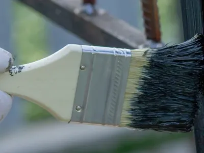 A worker paints a fence as part of an outdoor project by Paint‑Pro’s.