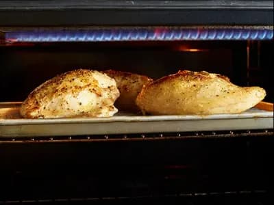 Seasoned chicken breast roasting on a sheet pan inside an oven.