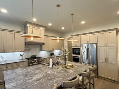 Luxury open kitchen and dining area with greige wainscoting, stone island, and brass chandelier pendants painted by OVO Painting in Atlanta