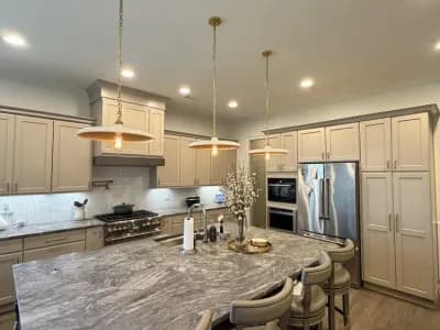 Luxury open kitchen and dining area with greige wainscoting, stone island, and brass chandelier pendants painted by OVO Painting in Atlanta